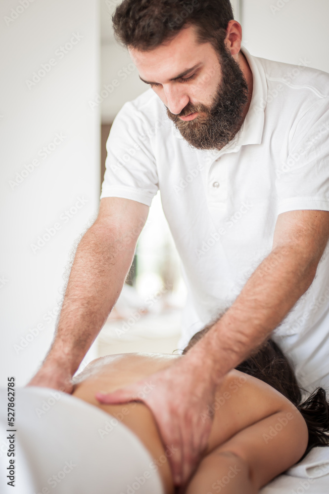 Female receives a back massage in a medical setting from a male masseuse, in spa salon - indoors Female receives a back massage in a medical setting from a male masseuse, in spa salon - indoors