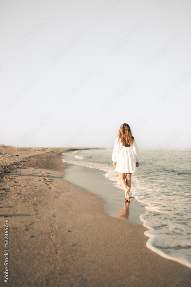 Young girl walking on the beach watching the sunset