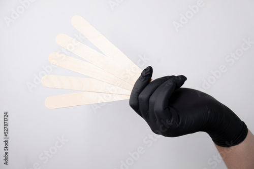 A woman's hand in a glove holds wooden spatulas for wax and sugar depilation. Depilation materials