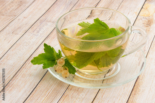 Still life of herbal tea from currant leaves in glass cup decorated fresh white currant berries and green leaves on wooden table