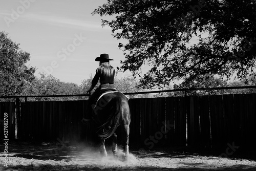 Western cowgirl riding horse in outdoor arena dust.
