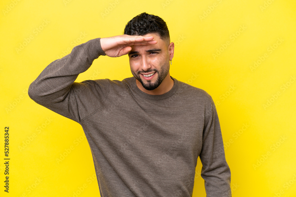 Young Arab handsome man isolated on yellow background looking far away with hand to look something Young Arab handsome man isolated on yellow background looking far away with hand to look something