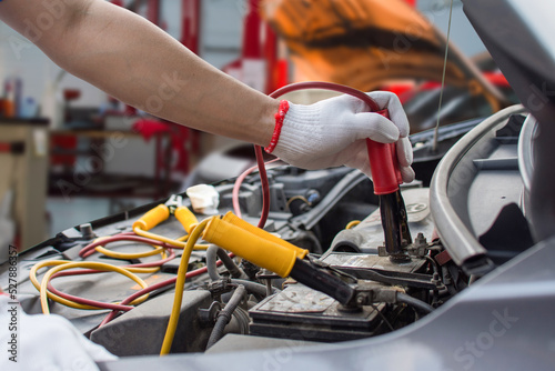 Mechanic holding red and black car battery repair jumper wires in maintenance center