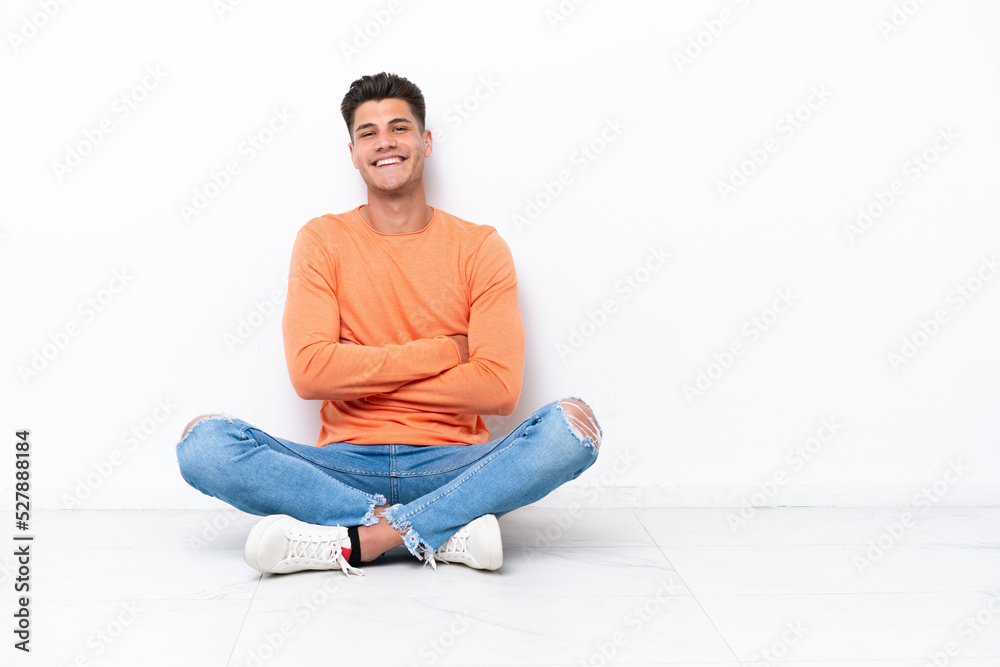 Young man sitting on the floor isolated on white background with arms crossed and looking forward