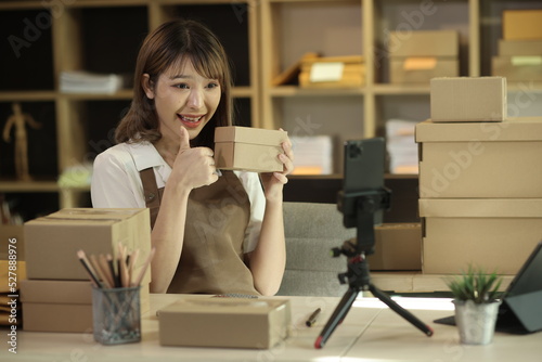 Asian young businesswoman using laptop computer online chat with packaging box, Business online influencer on social media concept, Online Selling, Online Shopping to market.