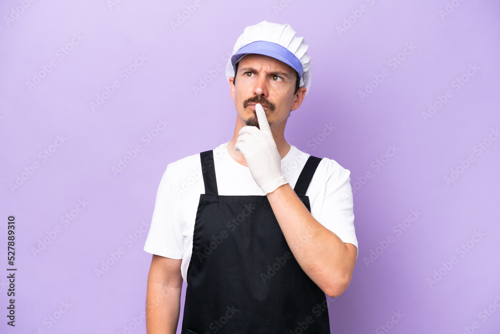 Fishmonger man wearing an apron isolated on purple background having doubts while looking up Fishmonger man wearing an apron isolated on purple background having doubts while looking up