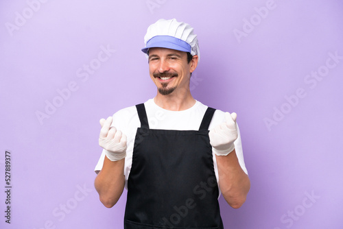 Fishmonger man wearing an apron isolated on purple background making money gesture