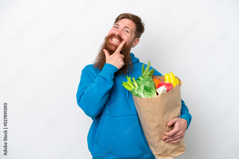 Redhead man with beard holding a grocery shopping bag isolated on white background happy and smiling Redhead man with beard holding a grocery shopping bag isolated on white background happy and smiling