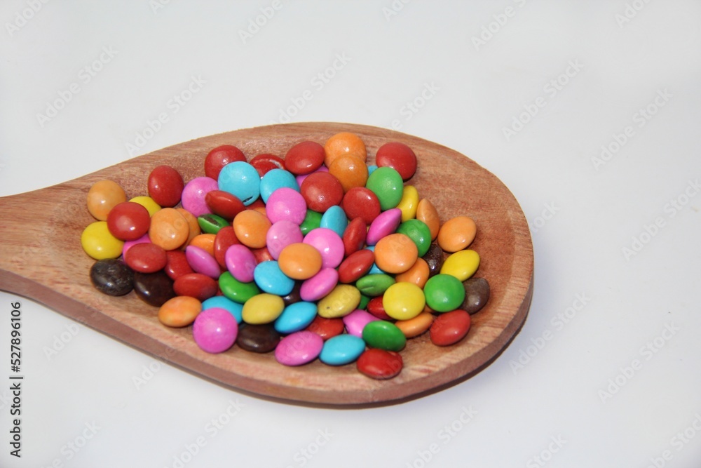 Chocolate candies covered in colored sugar in a wooden spoon isolated over a white background. Top view.