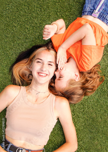 two girls lie on the grass and laugh, one girl whispers in the ear of the second girl and she smiles, sisters family vacation, secretly in the ear