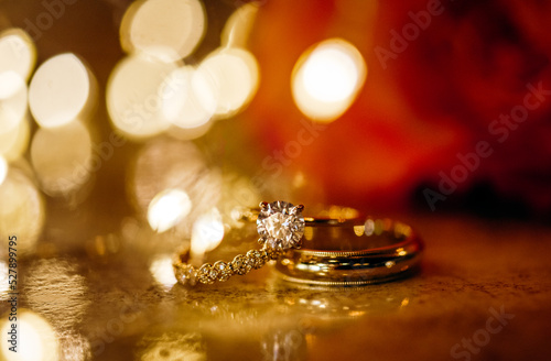 Gold wedding rings and engagement ring in front of boca lights with warm tones