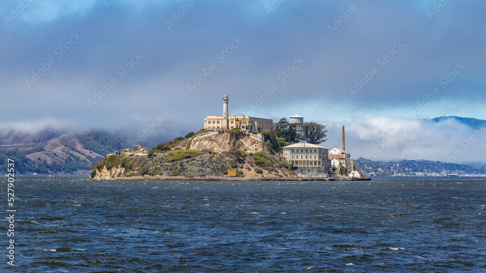 Wyspa Alcatraz otoczona błękitem wody. W tle chmury
