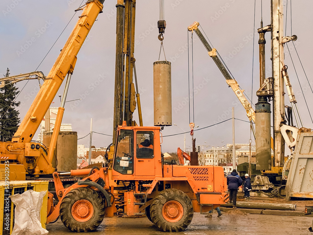 construction equipment at the overpass repair site. large concrete blocks are erected by cranes. an orange tractor for asphalt paving drives nearby on large wheels