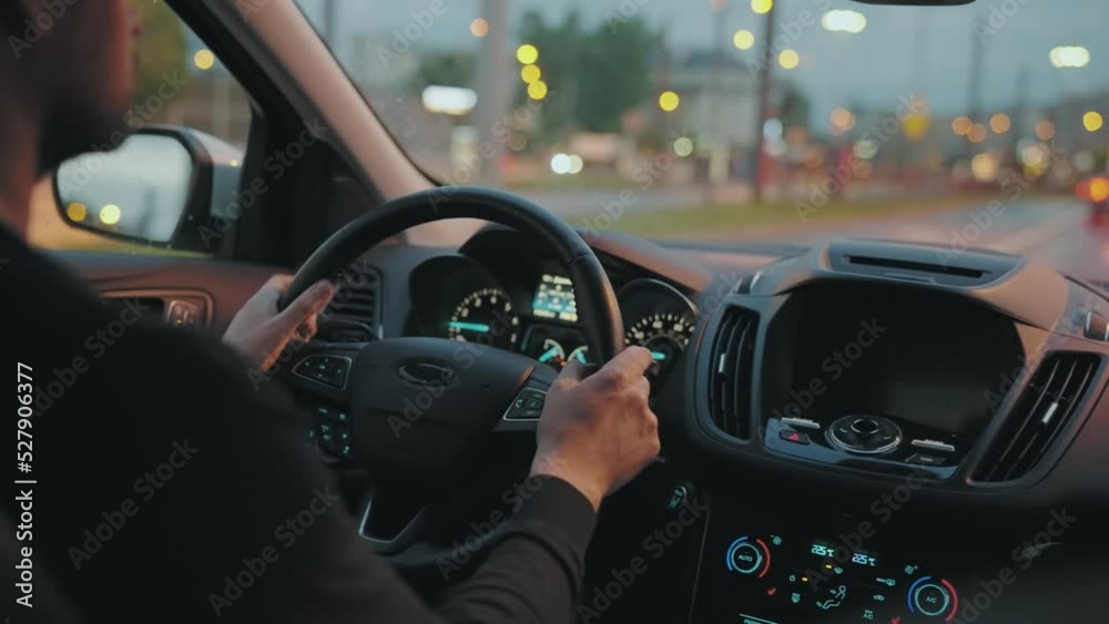 Man driving car through the streets of evening city. View from the back seat of the car Man driving car through the streets of evening city. View from the back seat of the car