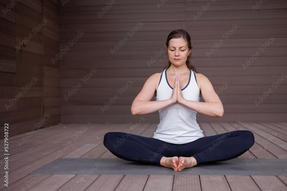 Fototapeta premium Beautiful strong muscular woman doing stretching on mat on terrace outdoors. Healthy young adult girl in sportswear stretch alone. Fit thin gimnast doing yoga, training on mat 