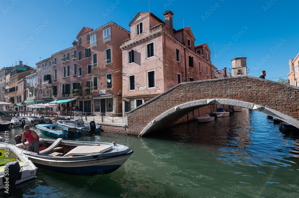 Vue typique d'un canal a Venise avec les reflest, les bateaux et un pont sur fond de ciel bleu
