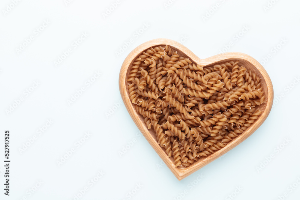 Whole grains fusilli pasta in a heart shaped wood bowl.