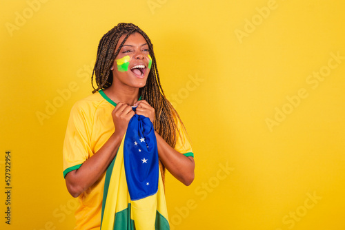 black woman young brazilian soccer fan. holding brazil flag, anxious, watching the match. photo