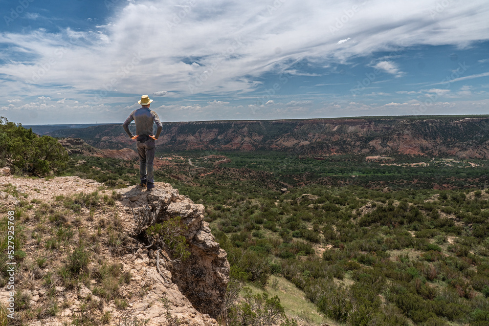 Mature man Caucasian hiker standing on the edge of a cliff looking down into a deep canyon, Rim Trail, Palo Duro Canyon State Park, Texas