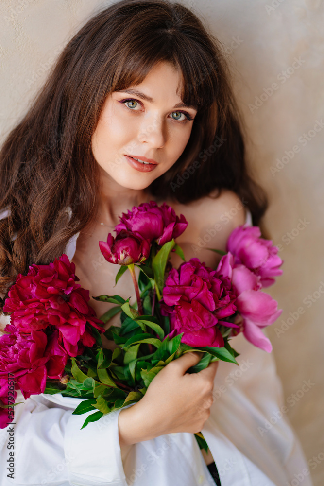 a beautiful young brunette woman in a white shirt with a bouquet of peonies.
