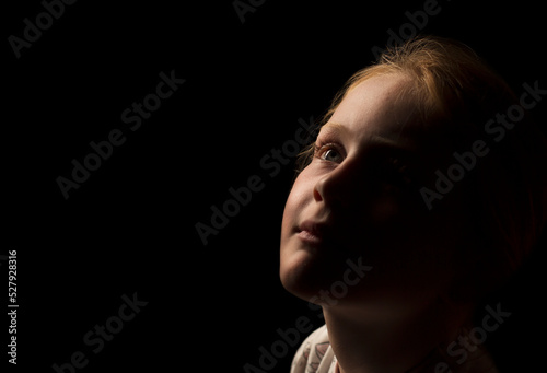 Young Caucasian girl looking upwards just away from the light with a very slight smile.