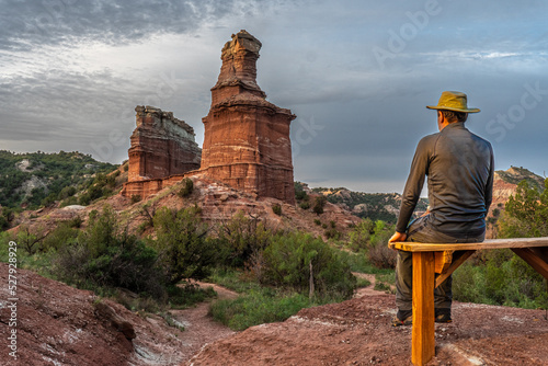 Mature man Caucasian hiker sitting on a wooden bench watching a magnificent large natural rock towers, The Lighthouse, Palo Duro Canyon State Park, Texas photo