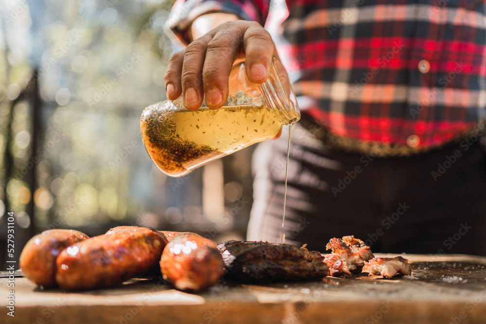 Crop man pouring dressing on grilled meat piece in garden Crop man pouring dressing on grilled meat piece in garden