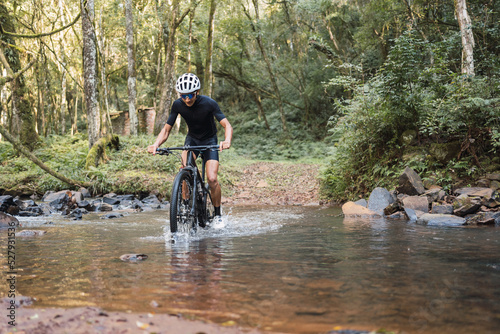 Cyclist riding bicycle in shallow river in forest