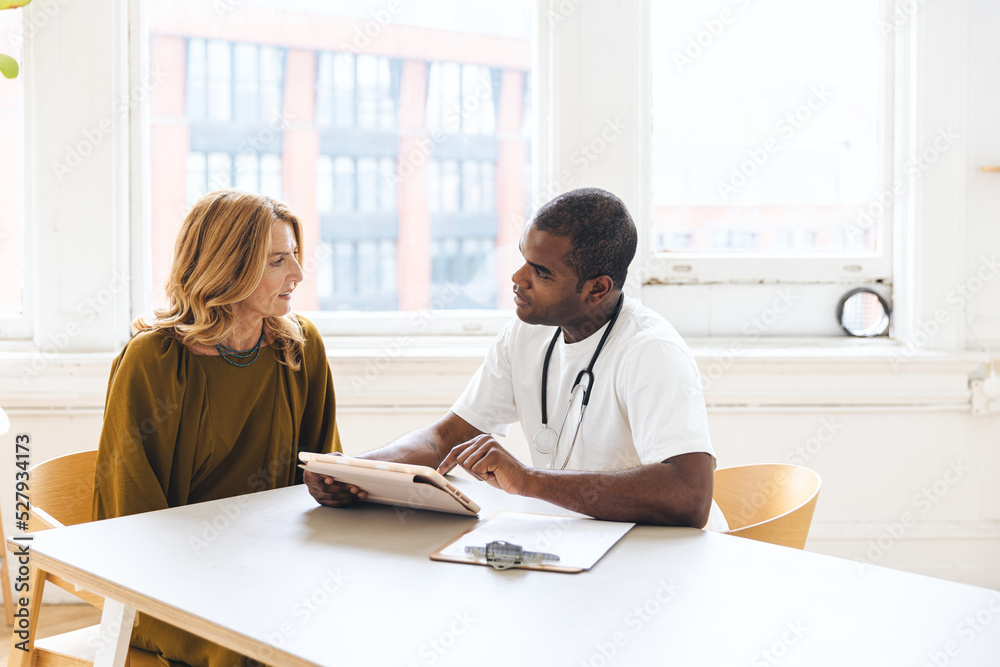 Doctor discussing with female patient over ipad record at clinic Doctor discussing with female patient over ipad record at clinic