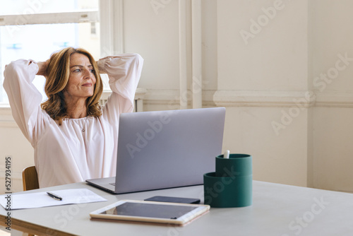 Contemplative businesswoman with hands behind head at creative office photo