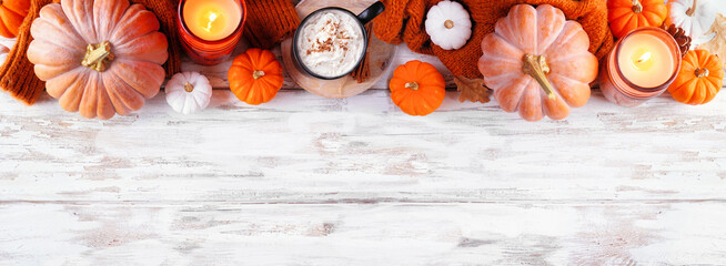 Cozy fall top border with pumpkins, leaves, sweater and pumpkin spice drink. Overhead view over a rustic white wood banner background.