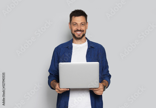Smiling man with laptop on light grey background