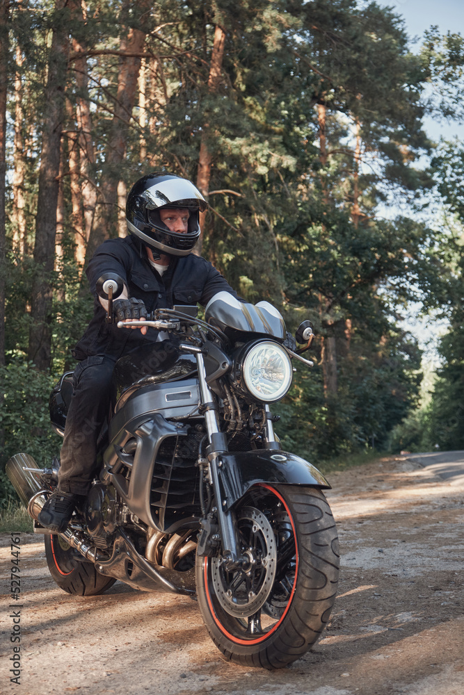 Young male biker in a helmet travels on a motorcycle alone, on a road in the forest