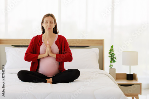 Pregnant woman sits in bed in her bedroom meditating alone in peace and happiness. The new mother resting by sitting down to chill out.