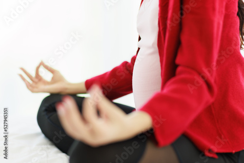 Pregnant woman sits in bed in her bedroom meditating alone in peace and happiness. The new mother resting by sitting down to chill out.