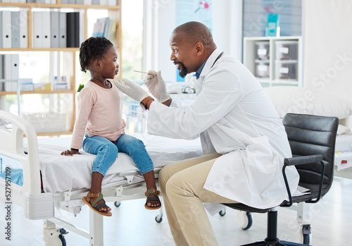 Doctor, mouth of child and black man helping little girl in checkup or consultation at a hospital. Medical male expert or pediatrician examining kid for throat infection, illness or sore in clinic. photo