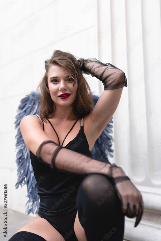 Beautiful girl with red lips in a black bodysuit, gloves and blue wings. Posing, looking at the camera Beautiful girl with red lips in a black bodysuit, gloves and blue wings. Posing, looking at the camera