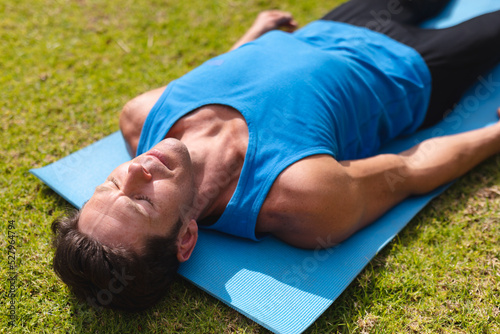 Young man in sportswear practicing shavasana on exercise mat in public park photo