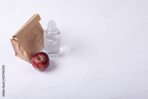 High angle view of paper lunch bag with apple and water bottle on white background along copy space
