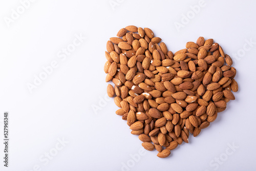 High angle close-up of almonds arranged in heart shape pattern on wooden white background