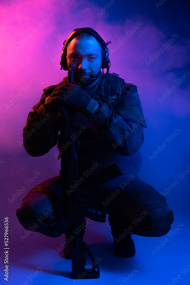 soldier in the studio on a blue background. a man in military uniform with a rifle or machine gun in colored light and smoke. military or airball player. blur
