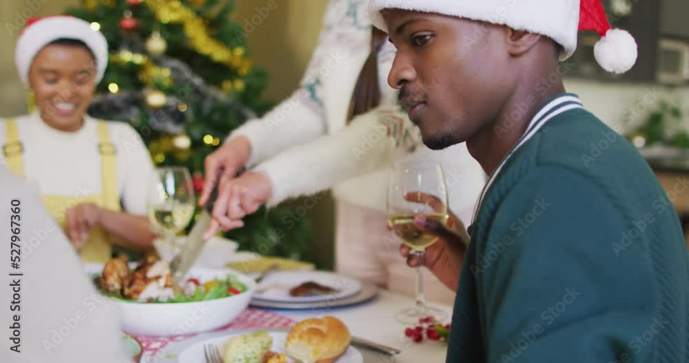Happy african american man in santa hat celebrating meal with friends at christmas time Happy african american man in santa hat celebrating meal with friends at christmas time