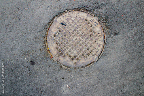 Old iron metal manhole cover sewer cap on the city street asphalt