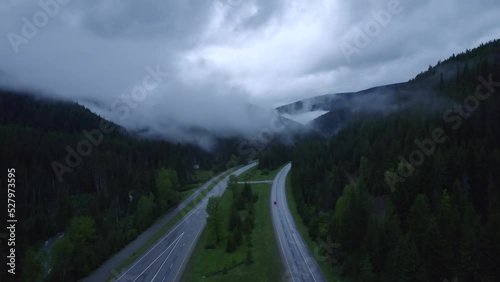 Aerial view of highway in mountain during sunset with fog. Tranquility mountain place. Cars and trucks is going on highway during a rainy weather in mountain.