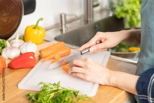 Asian young woman, girl or housewife hand using knife, cutting carrots on board, on wooden table in kitchen home, preparing ingredient, recipe fresh vegetables for cooking meal. Healthy food people.