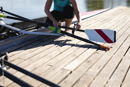 Low section of senior caucasian female rower attaching oars to the boat near the wooden dock