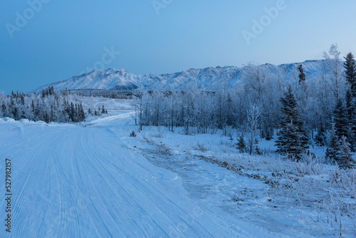 Chugach mountains in frosty winter twilight. Alaskan snow-covered forest road through the snow-covered taiga 