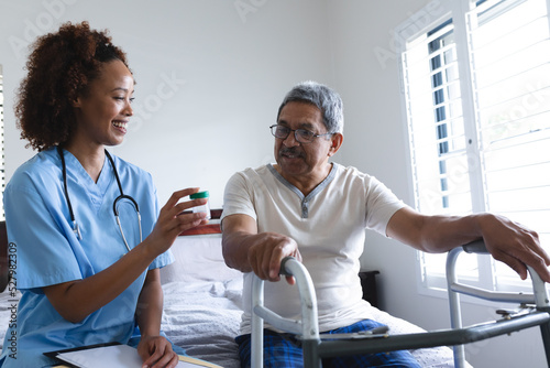 Mixed race female doctor giving pills to senior man at home