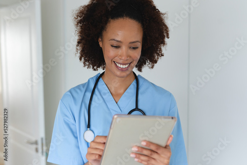 Mixed race female doctor home visiting using tablet and smiling