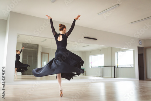 Caucasian female ballet dancer wearing a black dress and focusing on her exercise in a bright studio photo